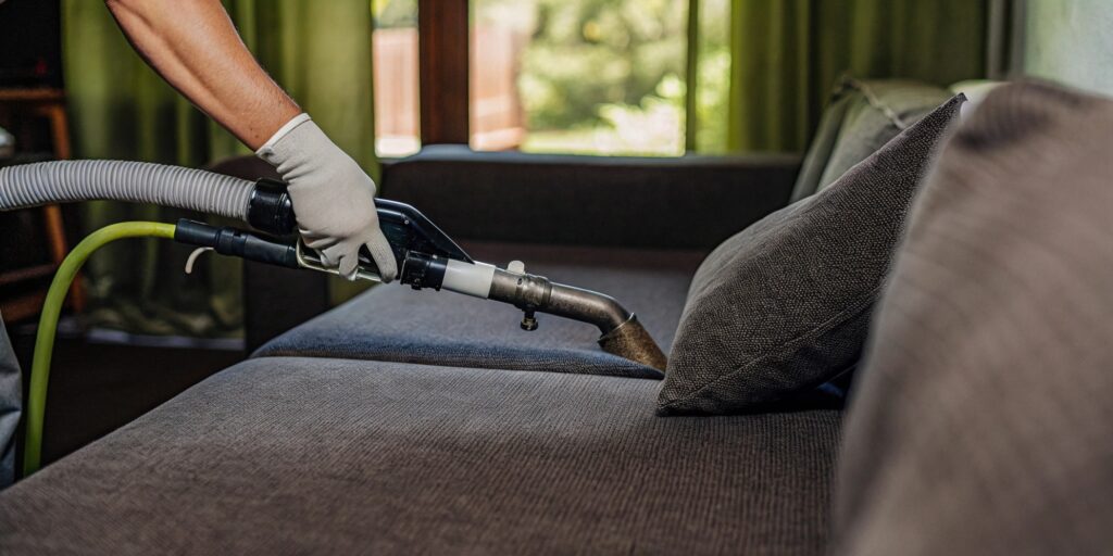 Technician performing professional upholstery cleaning on a fabric sofa using specialized extraction equipment in a modern home interior