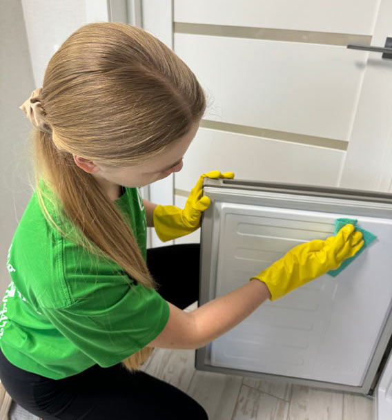 Zenvy cleaner in yellow gloves wiping the door of a refrigerator with a microfiber cloth - detailed appliance cleaning included in deep house cleaning service