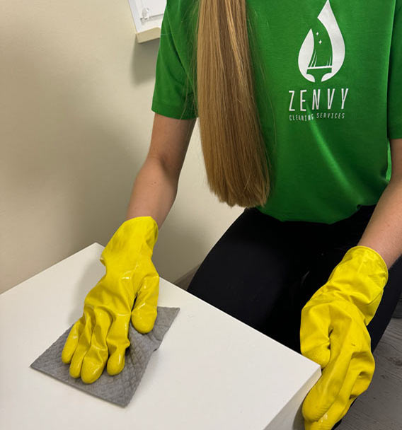 Zenvy cleaning specialist in green Zenvy uniform carefully wiping a white tabletop with a microfiber cloth and yellow rubber gloves
