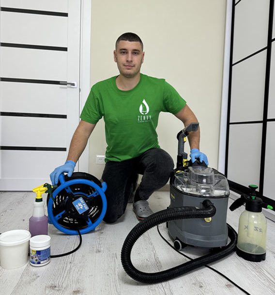 Zenvy cleaning technician in branded green uniform kneeling beside a Karcher extraction machine, spray bottles, and cleaning solutions - professional upholstery cleaning equipment in Toronto